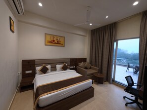 A hotel room with a large bed, a sofa, a small table, and a view of the outside. - Neelam Orchid  (Kanpur)