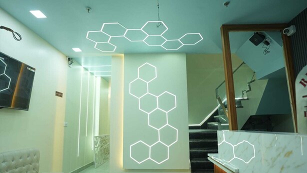 A modern interior with a hexagonal light installation, a staircase, and a marble reception desk. - Deep Palace Inn (Mathura)