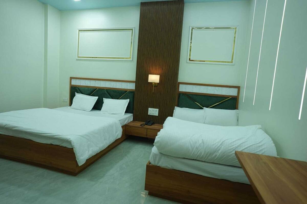 A hotel room with two single beds, wooden headboards, a nightstand with a lamp, and a large window with blinds.