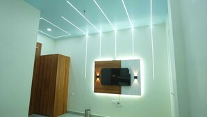 A modern bedroom with a wooden wardrobe, a wall-mounted TV, and recessed ceiling lighting. - Deep Palace Inn (Mathura)