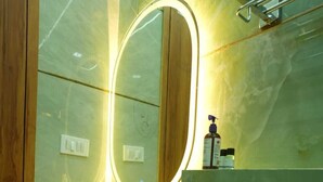 A modern bathroom with a marble sink, a large mirror with a light, and a shower area. - Deep Palace Inn (Mathura)
