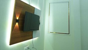 A modern room with a flat-screen TV mounted on a wooden panel, recessed lighting, and a plain door. - Deep Palace Inn (Mathura)