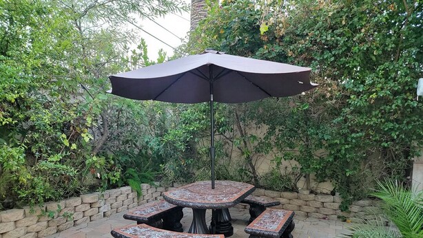 An outdoor patio with a round table and benches, surrounded by a stone wall and lush greenery.