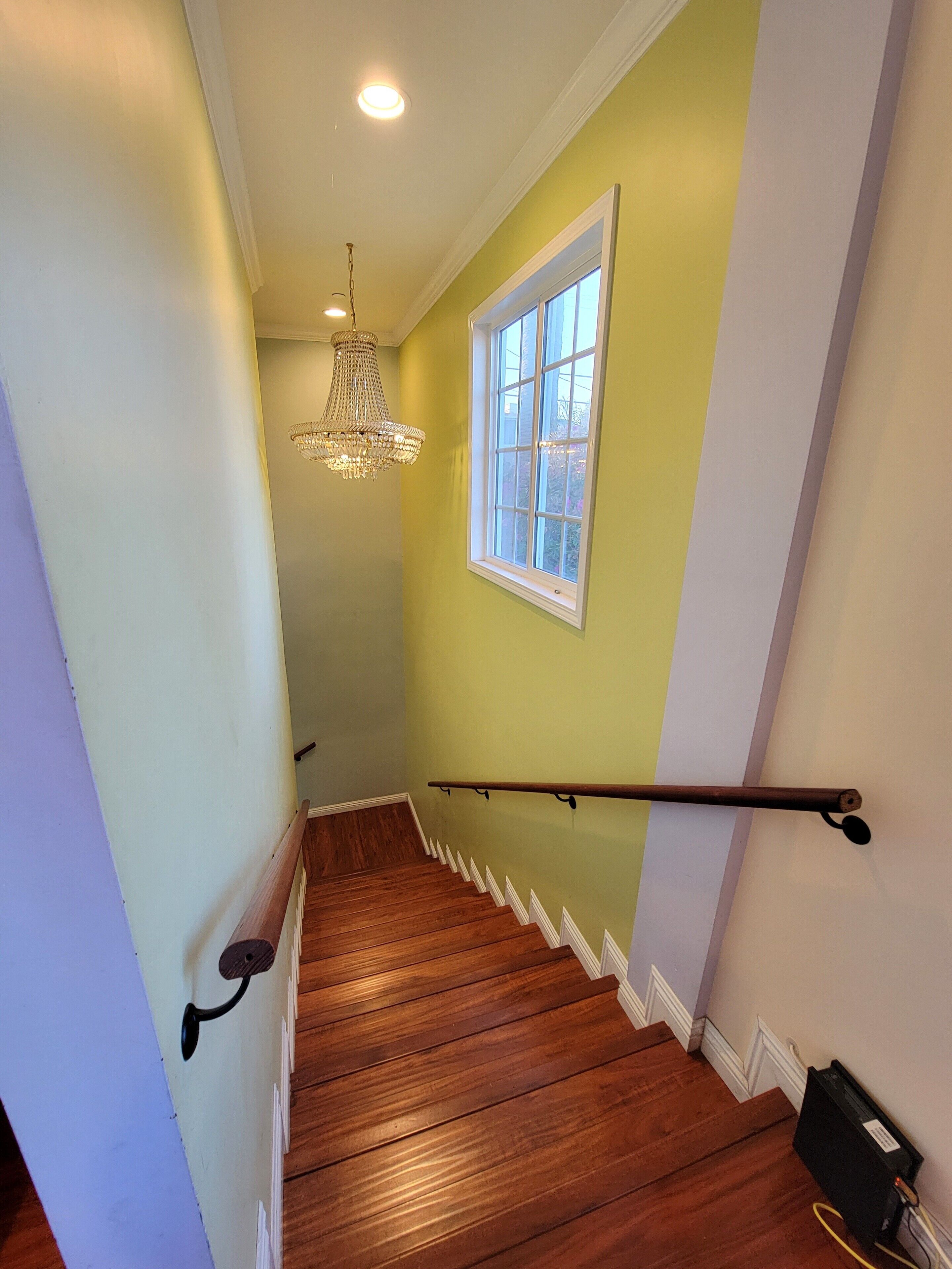 Una escalera de madera con barandilla, un candelabro y una ventana con vistas.