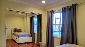 Un dormitorio con un espejo grande, una cama, una ventana con cortinas y vistas al exterior.