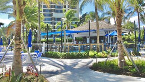 Un resort con zona de piscina, palmeras y un edificio con toldo azul.