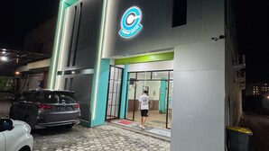A building with a large illuminated logo, a hexagonal tiled entrance, and parked cars. - Comfort Centre Residence Solo (Surakarta)