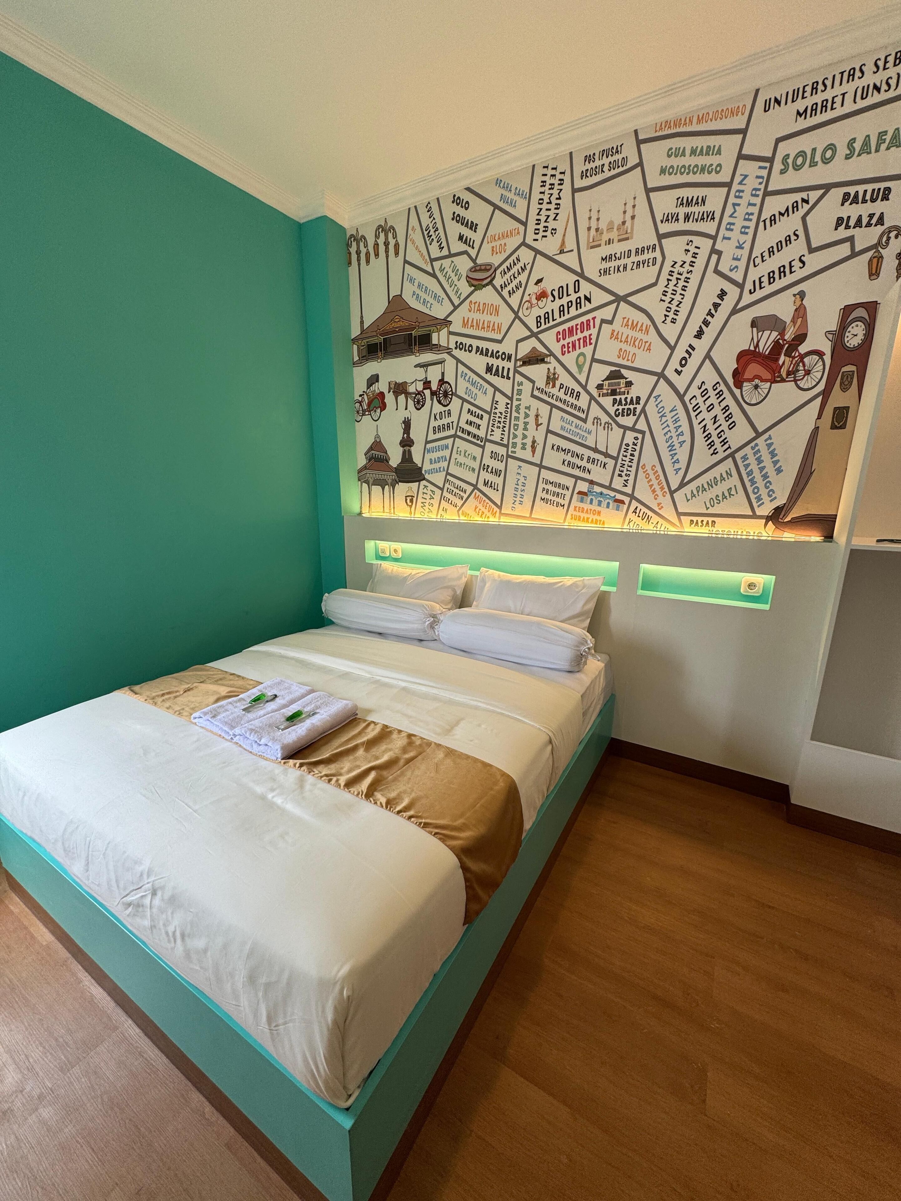 A hotel room with a bed, a map mural on the wall, and a teal accent wall.