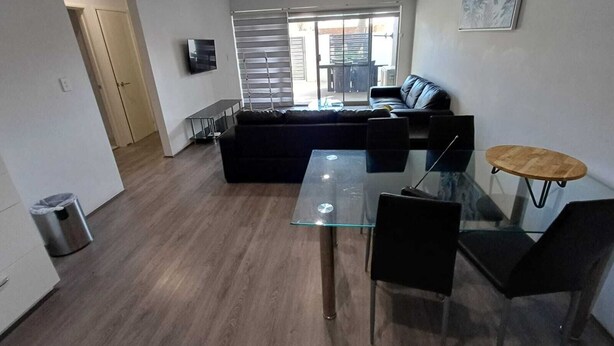A modern living room with a glass dining table, black sofas, and a small round table with chairs. - Nice Two Bedroom Apartment with courtyard/balcony in secure complex (Kelmscott)