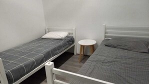 A small, single-room accommodation with two beds, one with a white headboard and the other with a grey headboard. There is a small round table between the beds. - Nice Two Bedroom Apartment with courtyard/balcony in secure complex (Kelmscott)