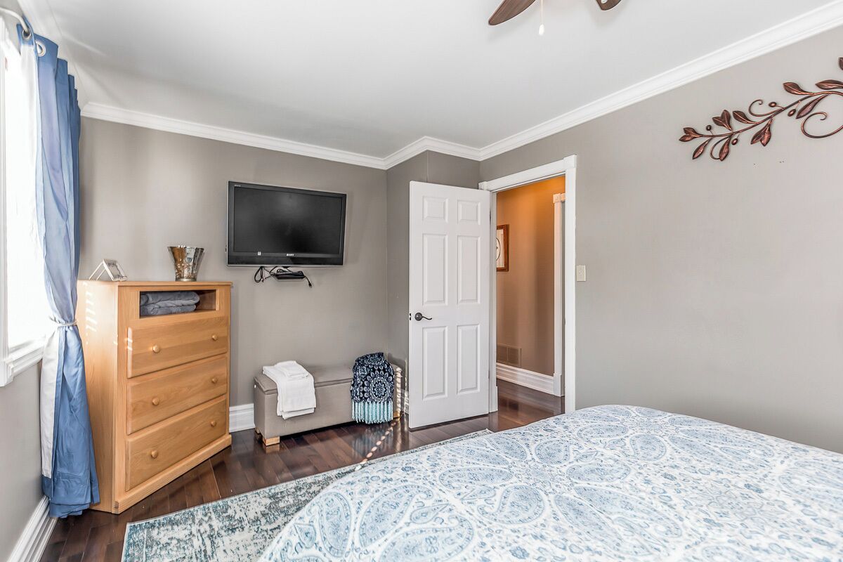 Un dormitorio con cama, cómoda, televisor y puerta que da a otra habitación.