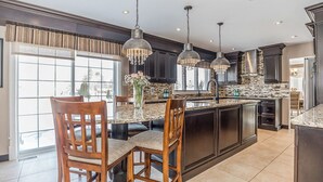 Une cuisine moderne avec des meubles de couleur sombre, un grand îlot central et des luminaires suspendus.