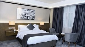Camera d'albergo con un letto, due lampade da comodino, una sedia, un tavolino e un quadro appeso al muro.