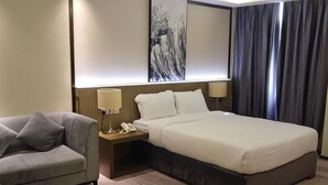 Una camera d'albergo con un letto grande, un divano, un comodino con una lampada e un quadro appeso al muro.