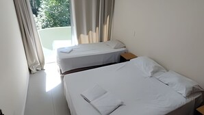 Ein Hotelzimmer mit zwei Einzelbetten, einem kleinen Holfnachtkästchen, einem Fenster mit Vorhängen und Blick auf Grün.
