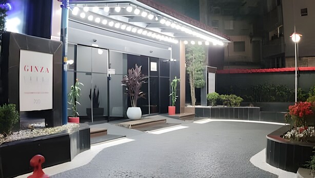 Ein moderner Hotel Eingangsbereich mit Glasfassade, einer gut beleuchteten Außenanlage und Pflanzkübeln.