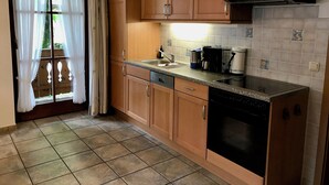 A kitchen with wooden cabinets, a black dishwasher, a stove, and a window with white curtains.