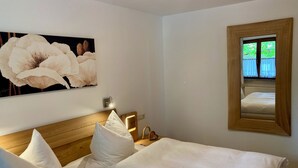A hotel room with a wooden headboard, white bedding, a large floral artwork on the wall, and a mirror reflecting the room.