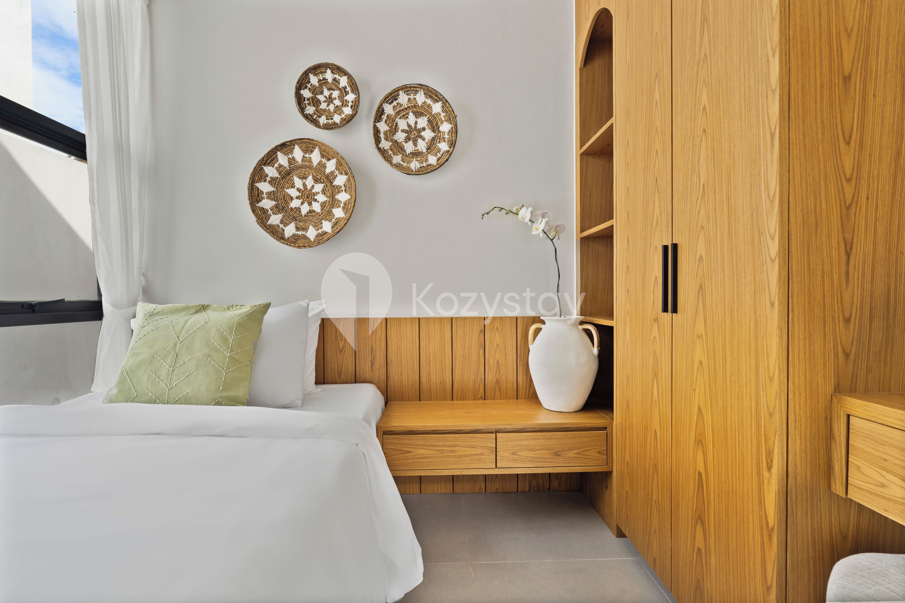 Een moderne slaapkamer met een bed, een houten garderobe, een witte vaas met bloemen en decoratieve wandkunst.