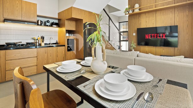 A modern kitchen with wooden cabinets, a dining area with a table set for four, and a television displaying the Netflix logo. - Tivara Villa by Kozystay - Jimbaran (Jimbaran)