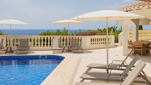 Zona junto a la piscina con sillones, sombrillas y vista al mar.