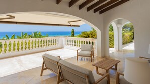 Un balcón amplio con vista al mar, amueblado con una mesa, sillas y una lámpara.