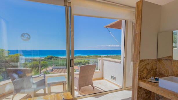Un balcón con vista al océano, jacuzzi, mobiliario de mimbre y un baño de mármol.