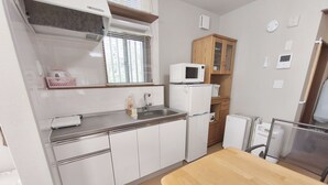 Une cuisine de taille réduite avec des meubles blancs, un four à micro-ondes, un réfrigérateur et une table en bois.