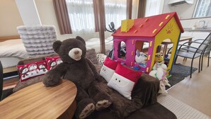 Une chambre d’hôtel accueillante, avec un grand ours en peluche, une maison de jeu et un lit parfaitement fait.