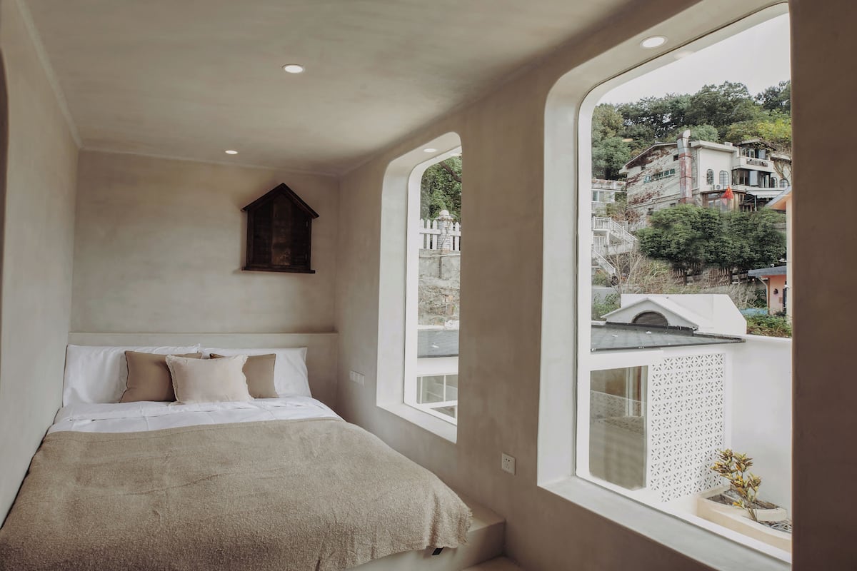 A bedroom with a large window, a bed with white bedding, and a wooden headboard.