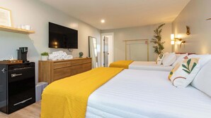 A hotel room with a bed, a TV, a minibar, a wooden dresser, and a plant. - Sage Deluxe Double Queen Studio at The Dogwood (Maggie Valley)