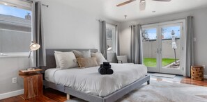 A bedroom with a bed, bedside tables, a lamp, a view through a glass door, and a small wooden stool.