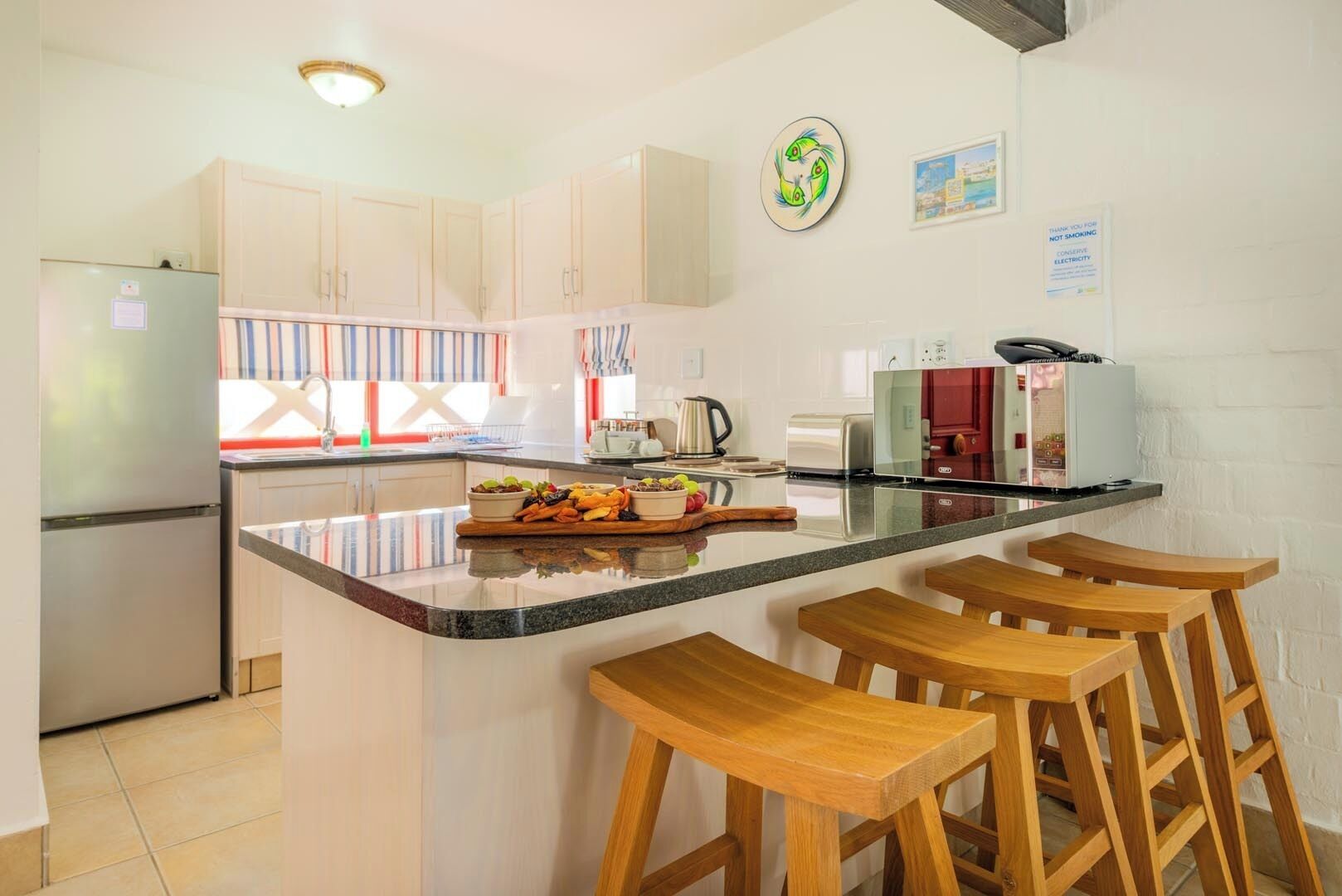 A modern kitchen with white cabinets, a central island with stools, a refrigerator, and a microwave.