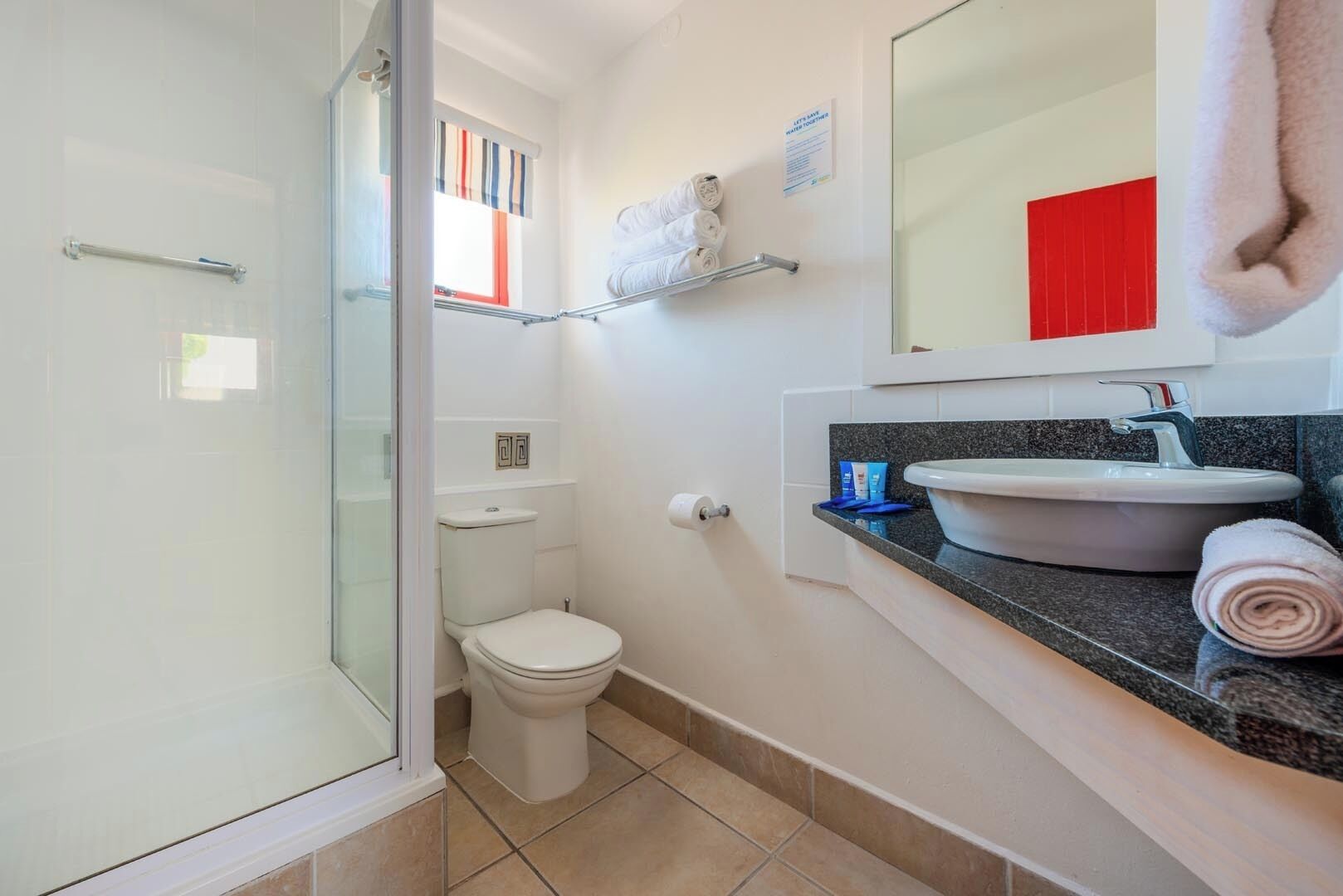 Un baño con cabina de ducha de vidrio, inodoro, lavabo con encimera de granito y toallero con toallas.