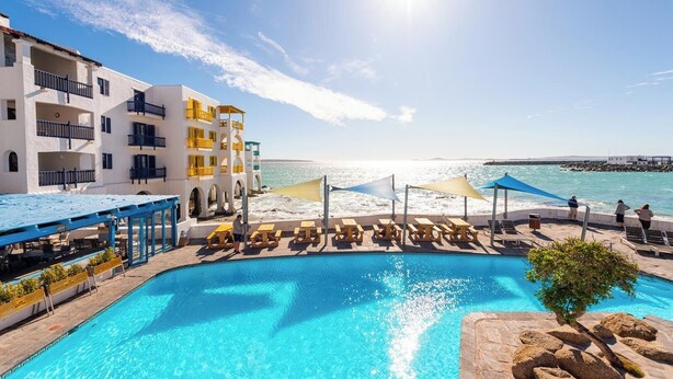 Zona de piscina con vistas despejadas al mar, un edificio con balcones y tumbonas.