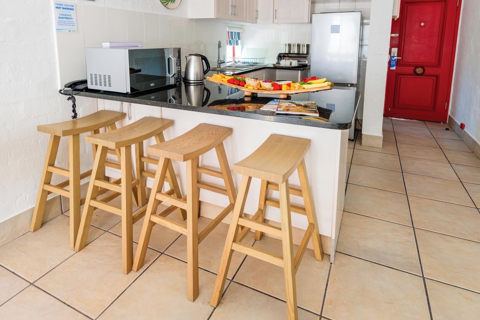 A kitchen with a black countertop, white cabinets, a red door, and four wooden stools.