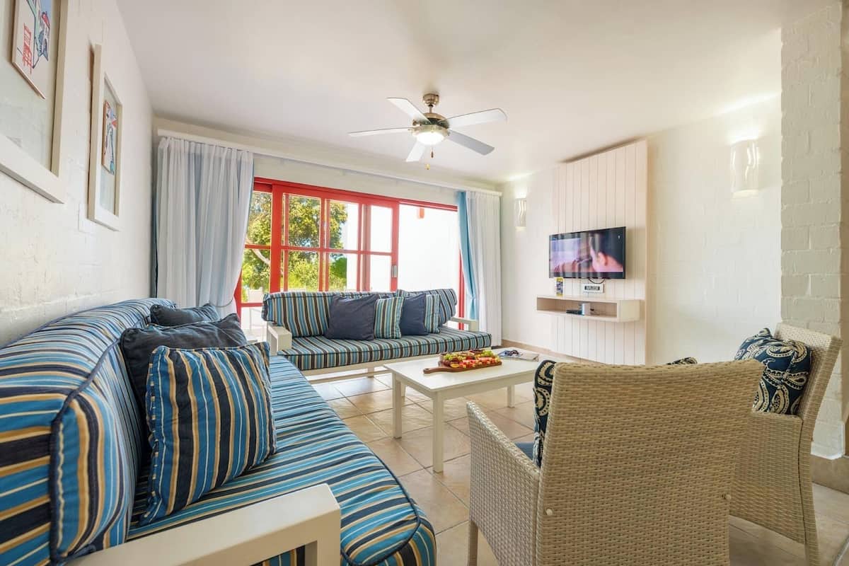 A living room with a sofa, a wicker chair, a coffee table, and a TV mounted on the wall.