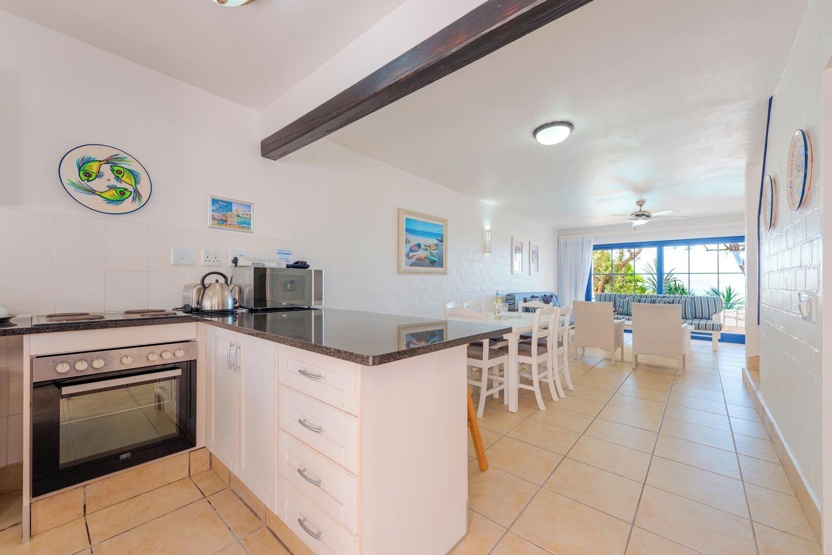 A modern kitchen with a central island, a dining area with a view, and a living space with a ceiling fan.