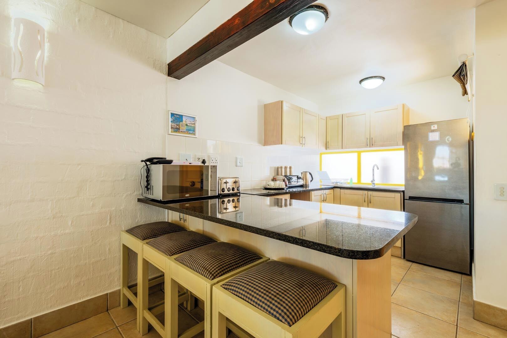 A kitchen with a central island, wooden stools, a refrigerator, and a microwave.