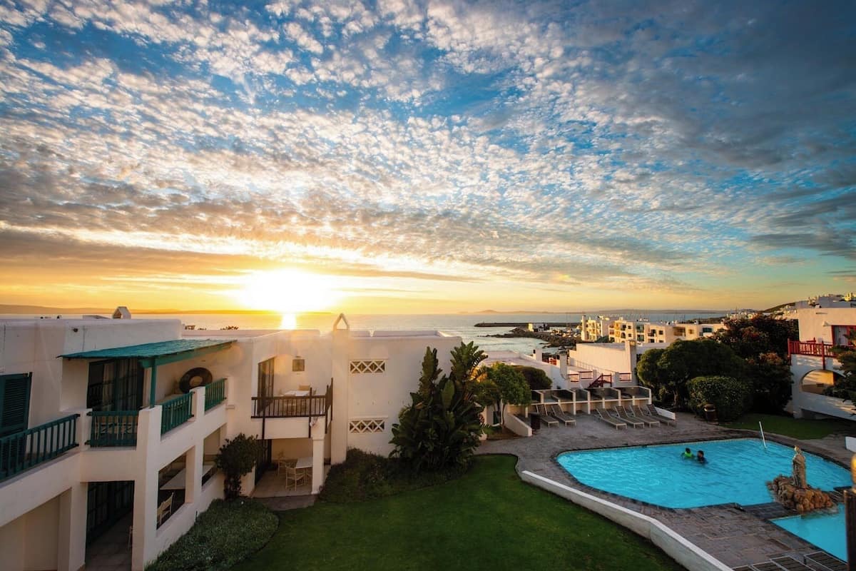 A resort with a swimming pool, a view of the sunset, and a clear sky.
