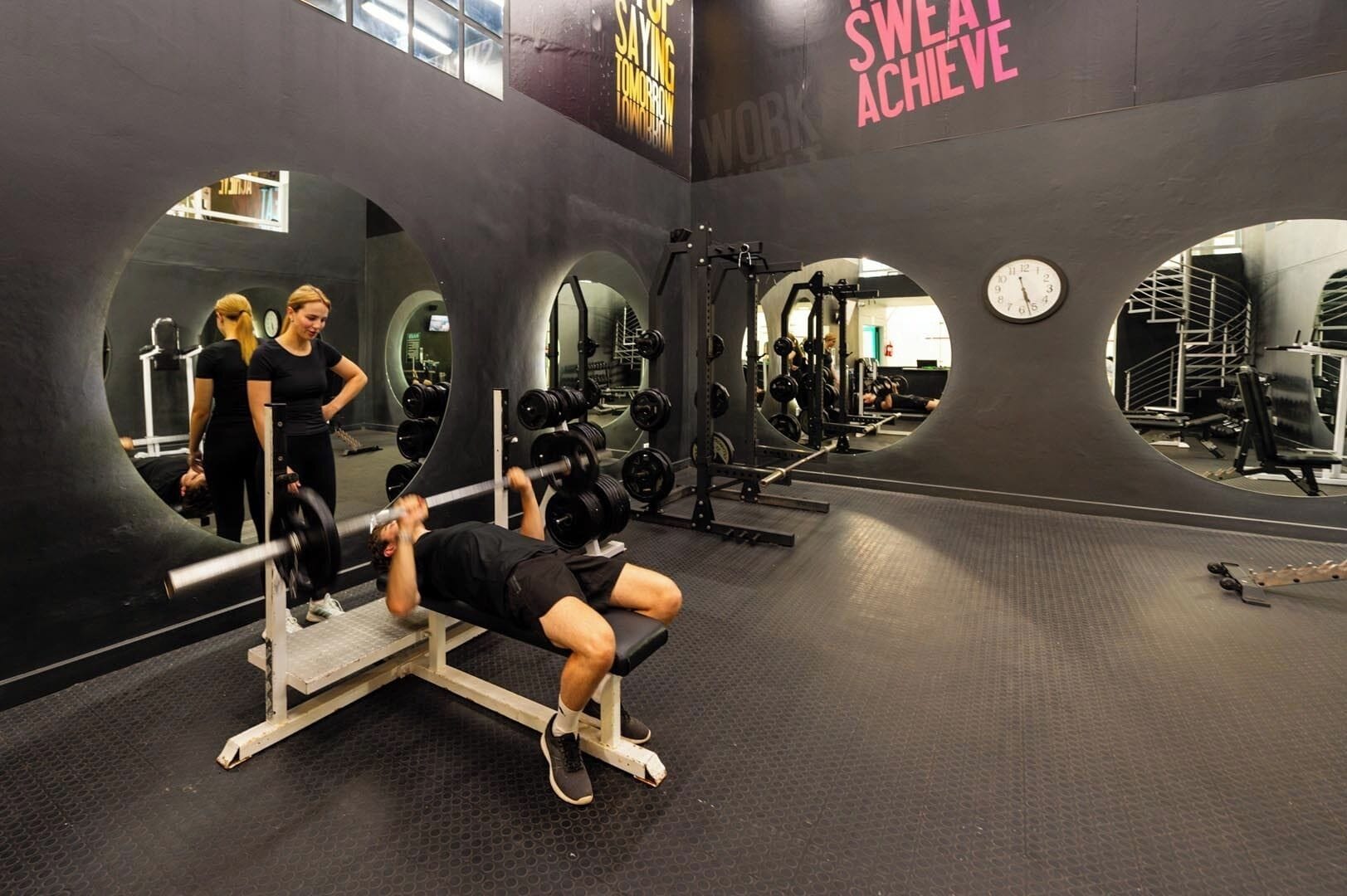 A gym with a mirrored wall, weightlifting equipment, and a motivational slogan.