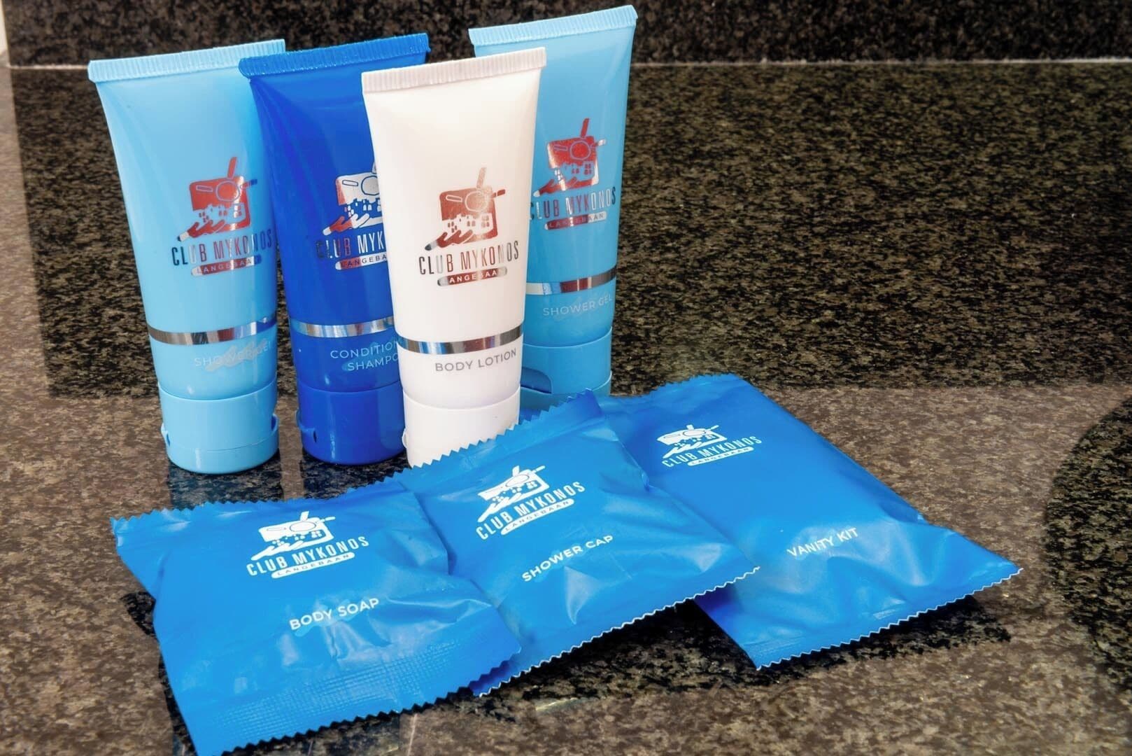 Une gamme de produits de soins corporels Club Mykonos comprenant un gel douche, une lotion pour le corps et un shampooing, ainsi que des savons pour le corps et des sachets de bonnets de douche.