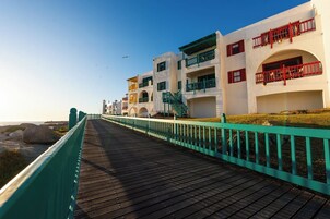 Un paseo marítimo de madera que conduce a una hilera de edificios blancos con balcones, algunos con barandillas rojas.