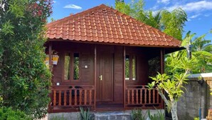 Ein Holzhaus mit Ziegeldach, einer Veranda mit Geländer und einem kleinen Gartenbereich mit Pflanzen und einem Betontritt, der zum Eingang führt.