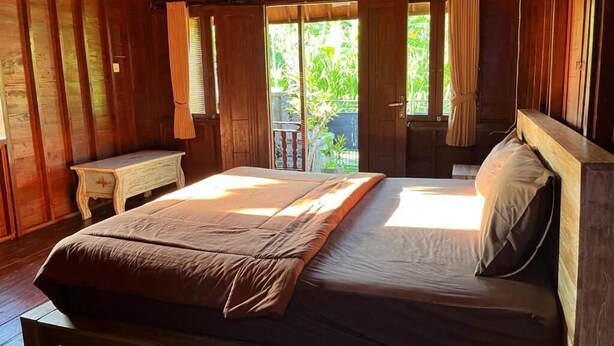 Ein Zimmer aus Holz mit einem großen Bett, einem kleinen Tisch und Blick ins Grüne.