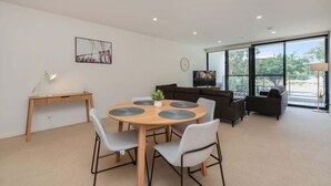 Un salon moderne avec une table ronde en bois, des chaises grises, un canapé marron foncé et un téléviseur posé sur un meuble.