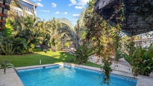 Una piscina amb un videt de rajola, envoltada de vegetació abundant i una paret de pedra.