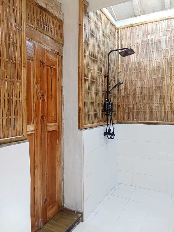 Un baño con ducha, puerta de madera y pared de bambú.