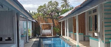 A swimming pool with a tiled deck, surrounded by buildings with a tropical architectural style.