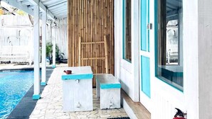 A covered outdoor area with a pool, stone flooring, wooden benches, and a fire extinguisher. - Kushak Bungalow Gili Trawangan (Gili Trawangan)